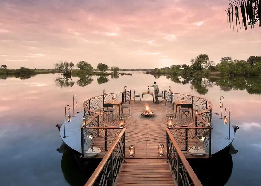 Elegant riverside deck at African Bush Camps Thorntree in Zambia, featuring lantern-lit seating and a central firepit overlooking the river, offering a luxury African safari atmosphere.