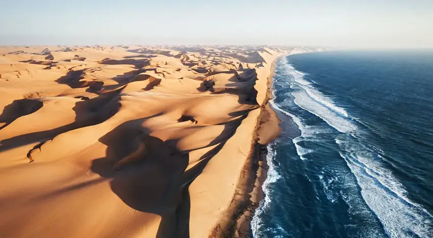 Aerial view of the Skeleton Coast in Namibia, where towering desert dunes meet the crashing waves of the Atlantic Ocean, captured during an African safari adventure.