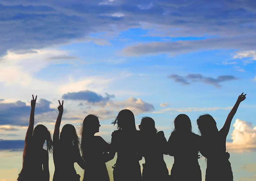 Silhouette of a group of women raising their arms in celebration against a dramatic blue and cloudy sky during an African safari adventure.