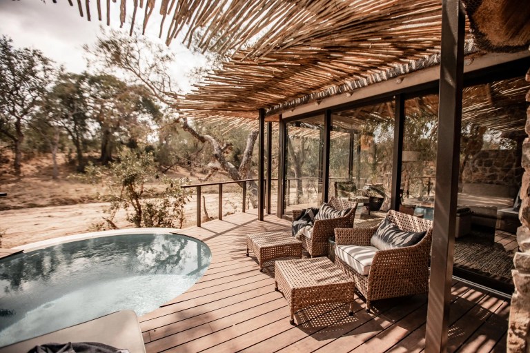 Tranquil deck of a luxury safari lodge overlooking an outdoor pool. Wicker furniture and a woven roof provide shade, perfect for relaxing in the African sun. The safari lodge offers luxury accommodation with scenic views.