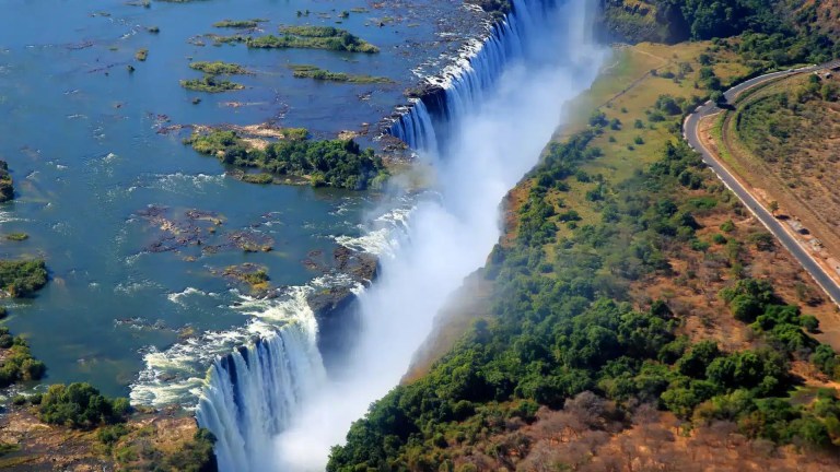 Aerial view of the majestic Victoria Falls, a breathtaking natural wonder in Africa, showcasing the powerful Zambezi River cascading over a vast cliff, creating a misty spray. This iconic landmark is a must-see for any Victoria Falls safari guide.